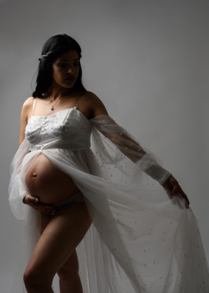 Elegant maternity photo in sheer white gown with soft lighting